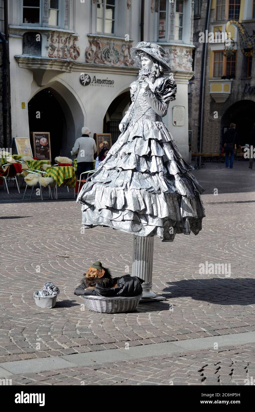Innsbruck, Austria - March 02, 2011: Unidentified silver coloured woman with dog as street performer, part of Helbling House behind Stock Photo