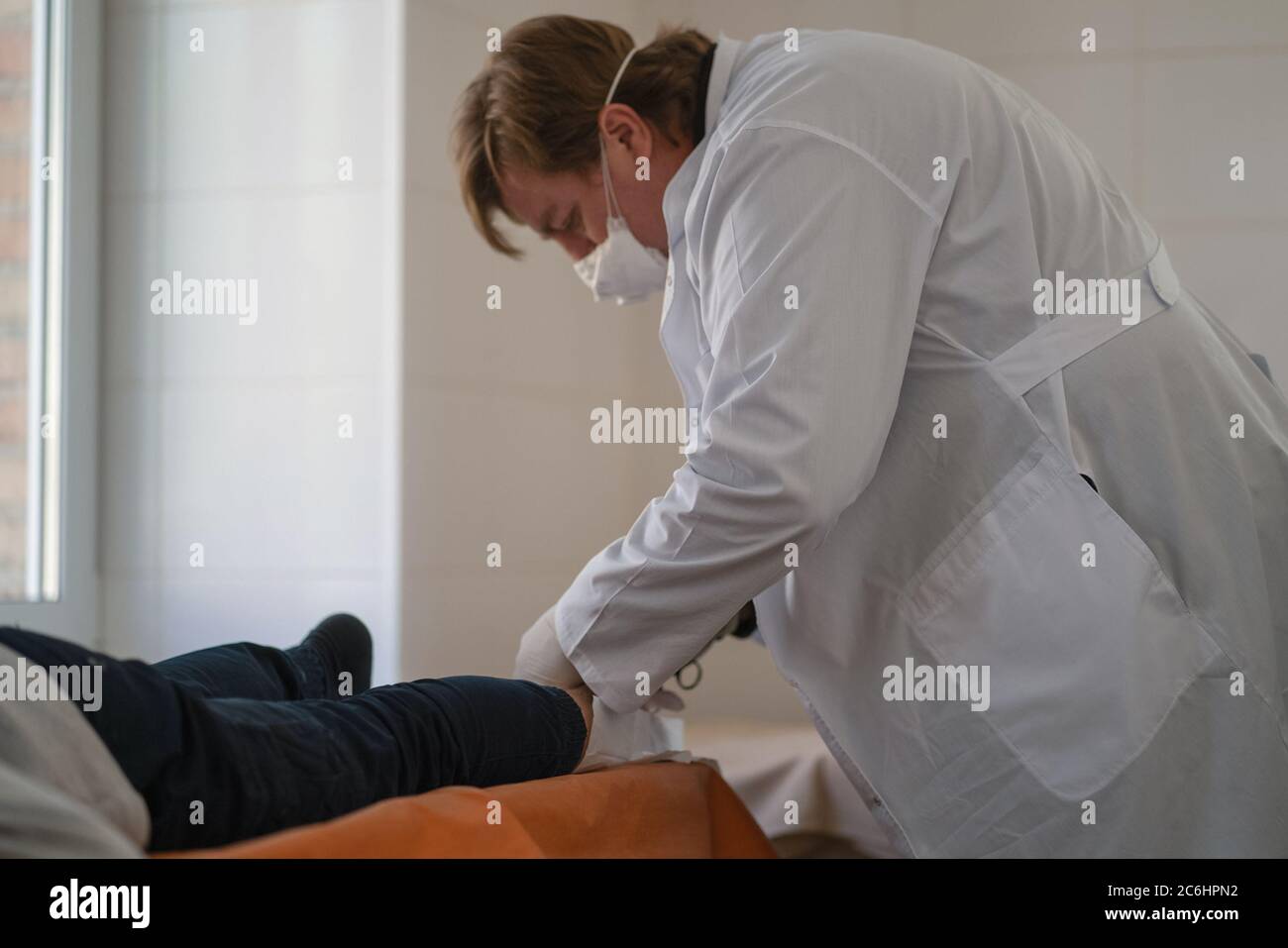 Doctor surgeon examining his patient leg. Medic inspects of patient lying on couch examining his leg. City Hospital. May, 2020, Brovary, Ukraine Stock Photo
