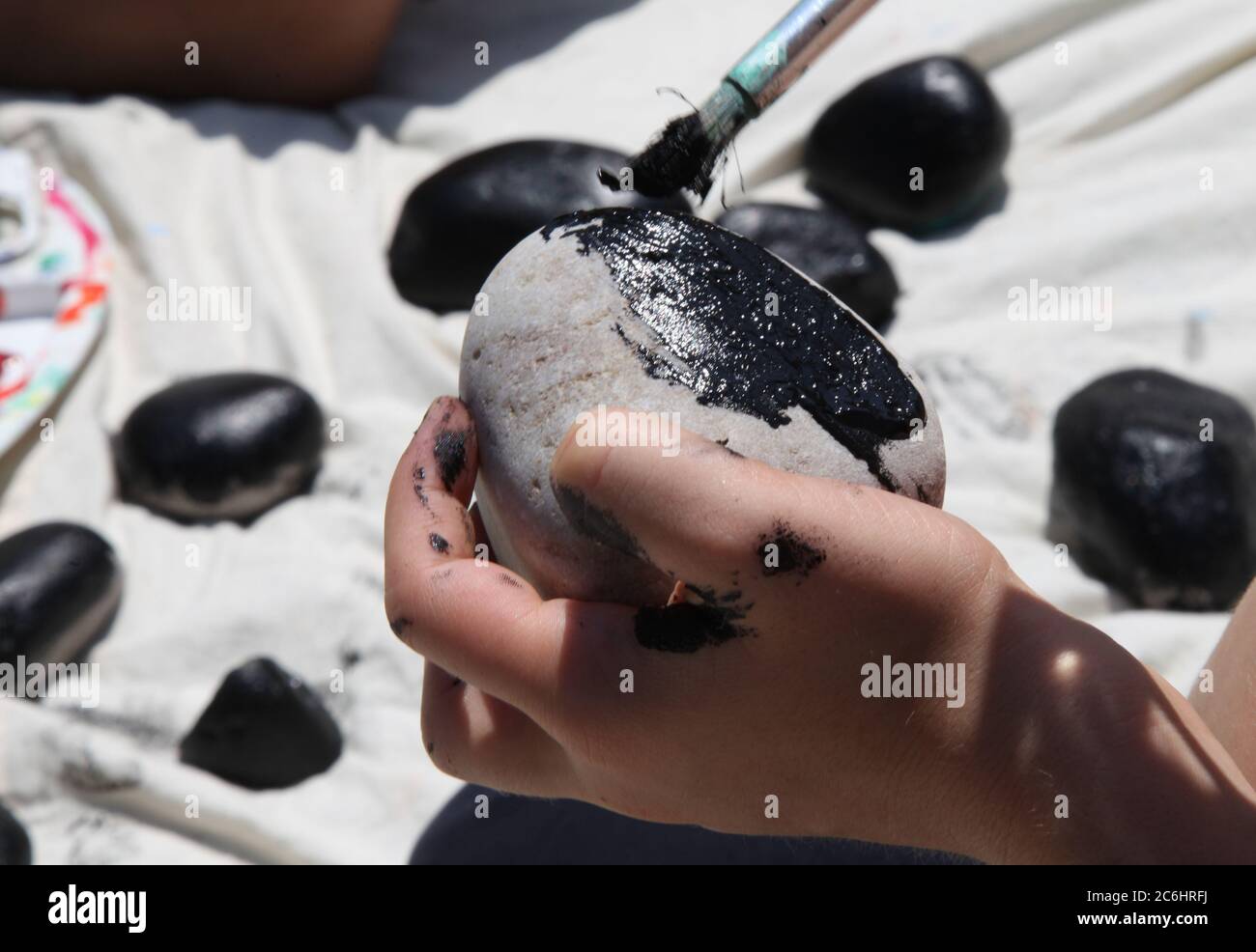 A child's hand rock painting holding a paintbrush children painting rocks, black paint on to rocks for Halloween outside, 2020 Stock Photo
