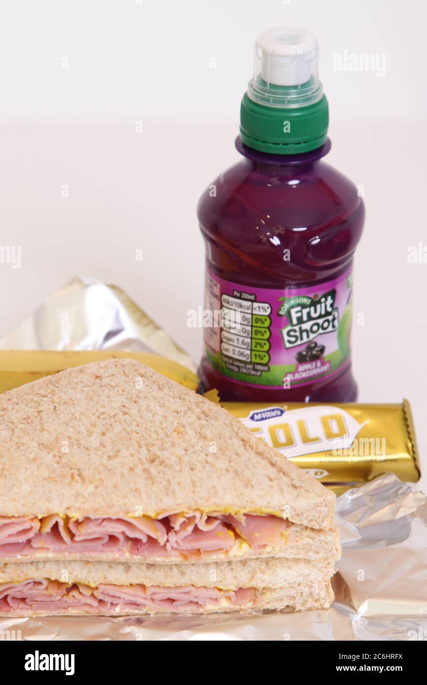 A UK school packed lunch box contents. Ham and mustard sandwich with Gold chocolate bar and Fruit Shoot. Stock Photo