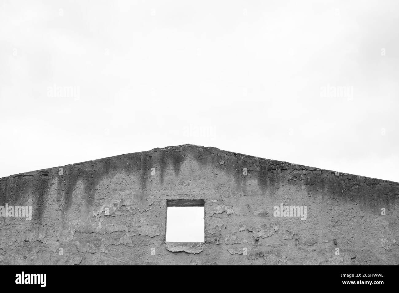 Black and white minimalistic geometric composition of abandoned house - unplastered gable wall with hole for window. Building is ruined and without ro Stock Photo