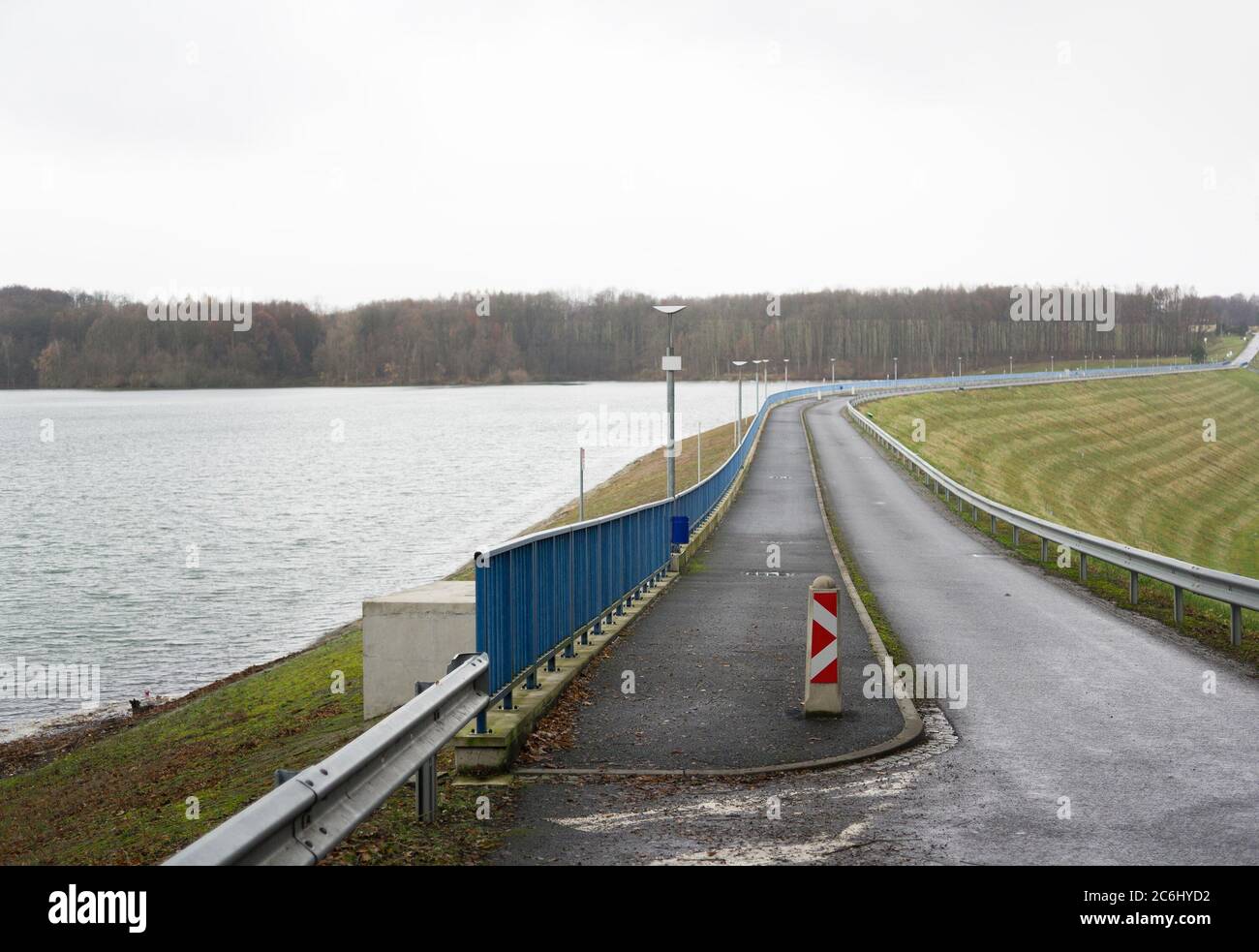 Straight narrow road and sidewalk by the water, artificial lake or dam. Ugly autumn / fall weather Stock Photo