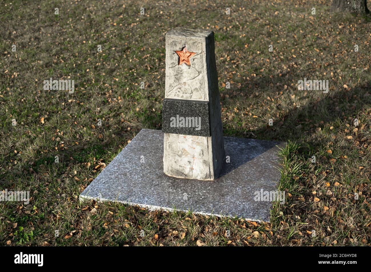 Memorial and grave of unknown soviet soldier from red army. Gravestone with red star. Grass and leaves around place Stock Photo