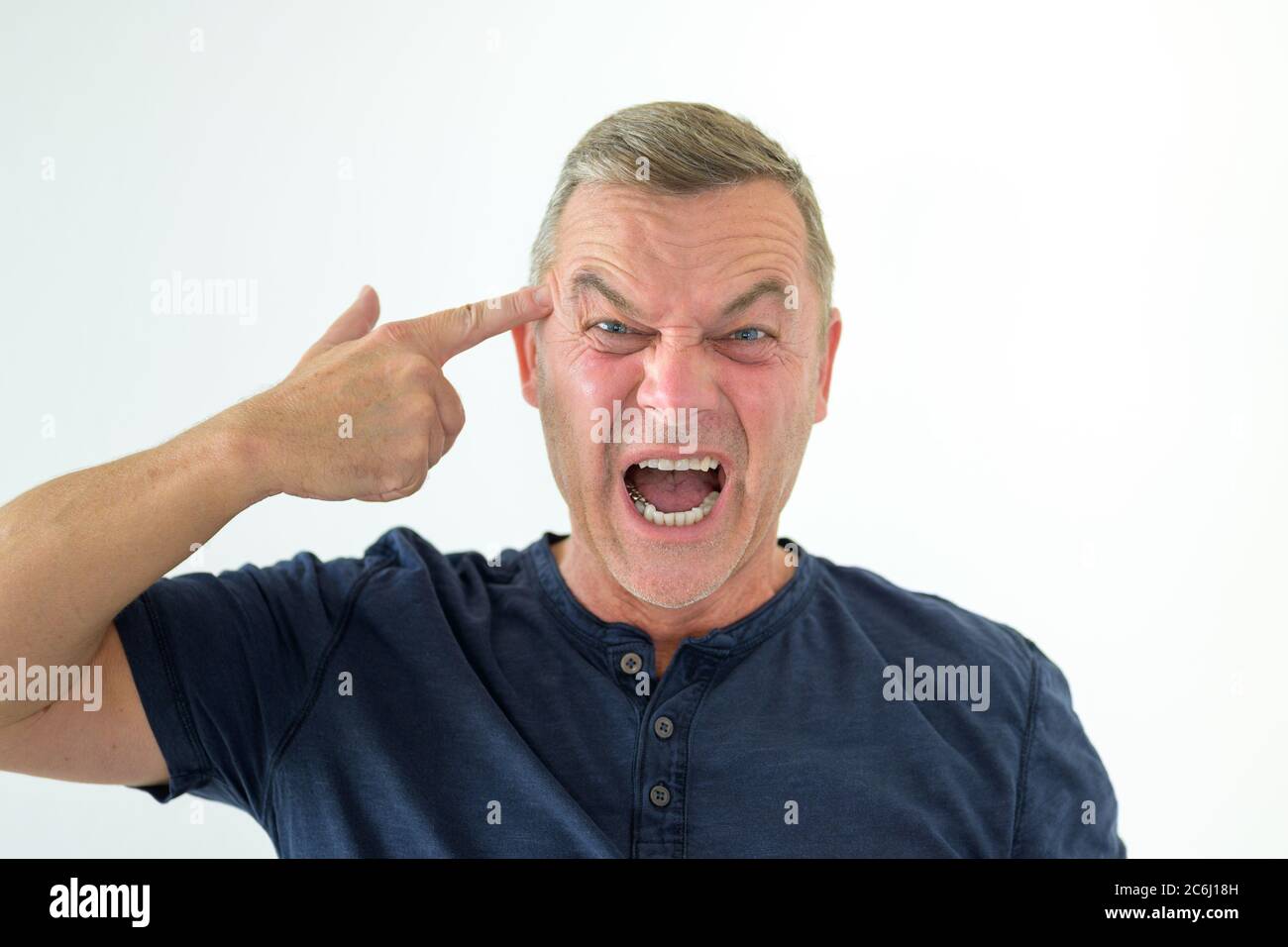 Angry man making a gun gesture pointing to his head as he yells at the camera isolated on white Stock Photo