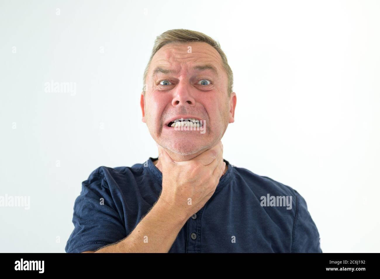 Angry frustrated man grabbing at his throat while gnashing his teeth and glaring at the camera in a head and shoulders portrait on white Stock Photo
