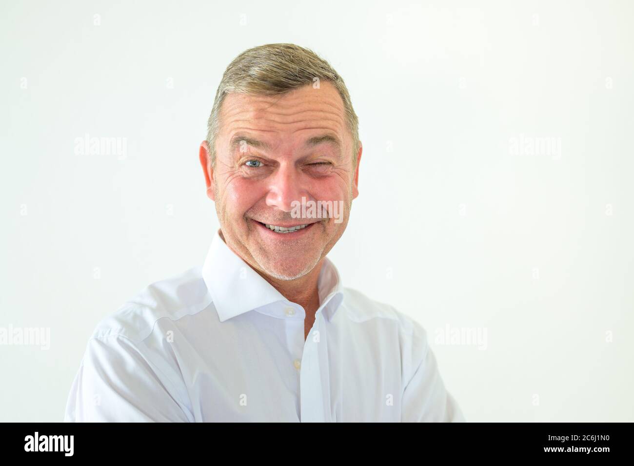 Middle-aged man grinning with glee and winking at the camera in a frontal head and shoulders portrait on white Stock Photo
