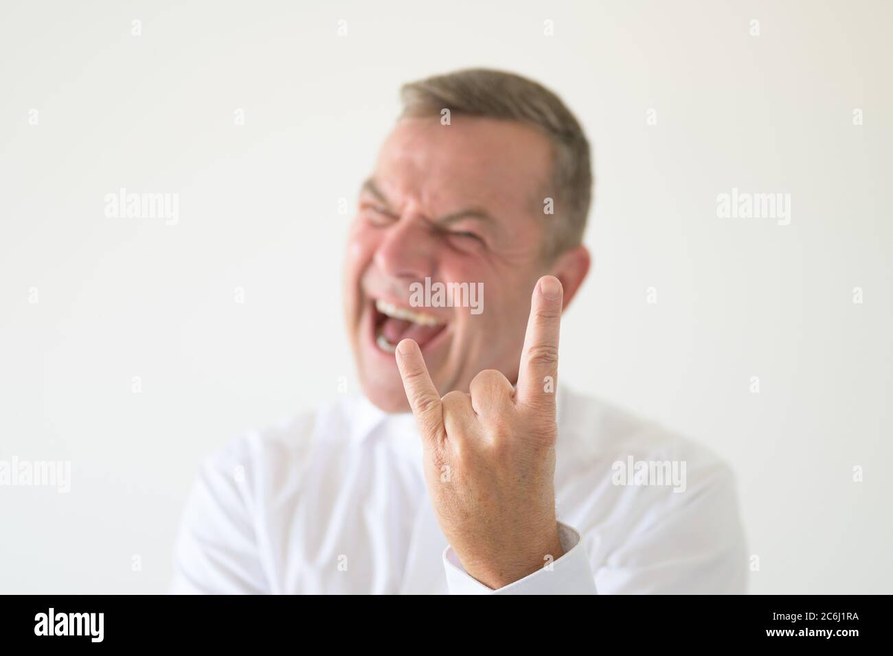 Angry middle-aged man making a Horns gesture with focus to his hand in a head and shoulders portrait on white Stock Photo
