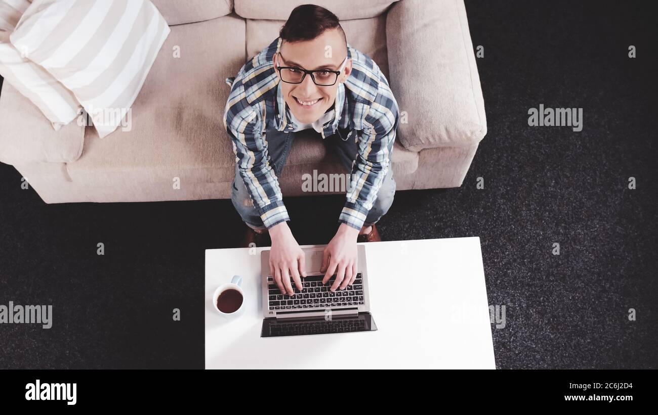 Cheerful man looking up typing on laptop. Freelanser man works at cozy home workplace. High angle view. Tinted image Stock Photo