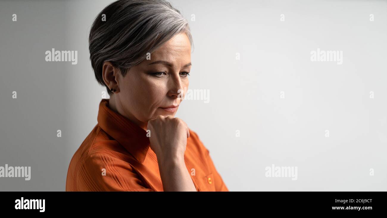 Thoughtful woman looks away touching chin with hand. Pensive mature lady thinking alone. Loneliness concept. Depression concept. Blank with empty Stock Photo
