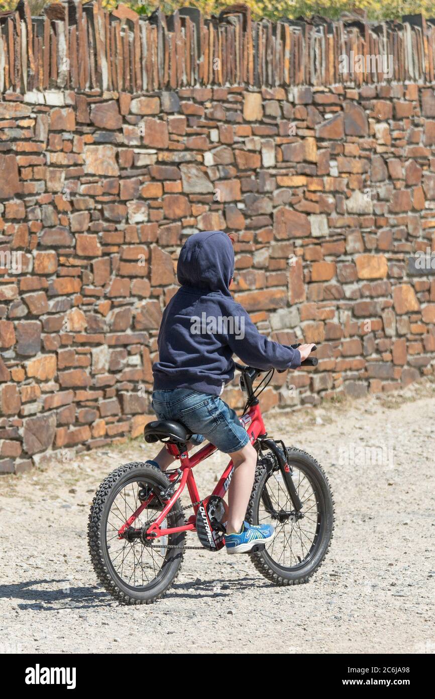 A young boy wearing a hoodie riding his bicycle. Stock Photo
