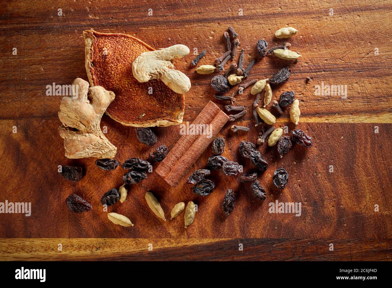 A mix of dry mulling spices (ginger, orange rind, raisins, cloves, cinnamon stick, cardamom pods) on wooden board. Stock Photo