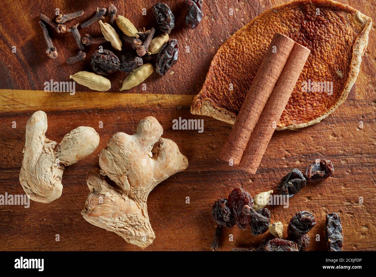 A mix of dry mulling spices (ginger, orange rind, raisins, cloves, cinnamon stick, cardamom pods) on wooden board. Stock Photo