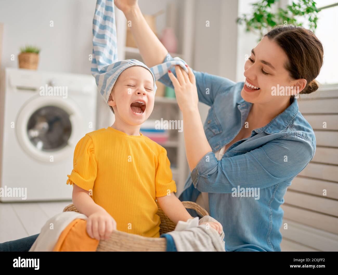 Beautiful young woman and child girl little helper are having fun and smiling while doing laundry at home. Stock Photo