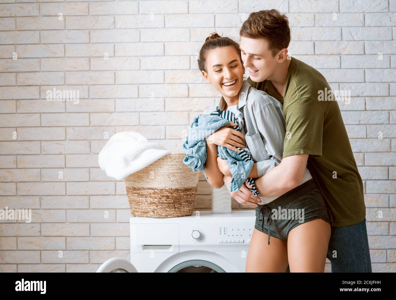 Beautiful young loving couple is smiling while doing laundry at home ...