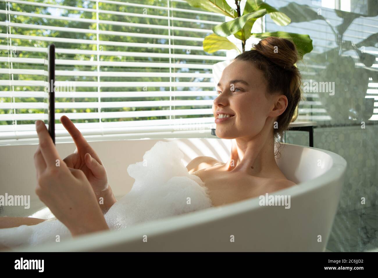 Woman using smartphone in a bathtub Stock Photo