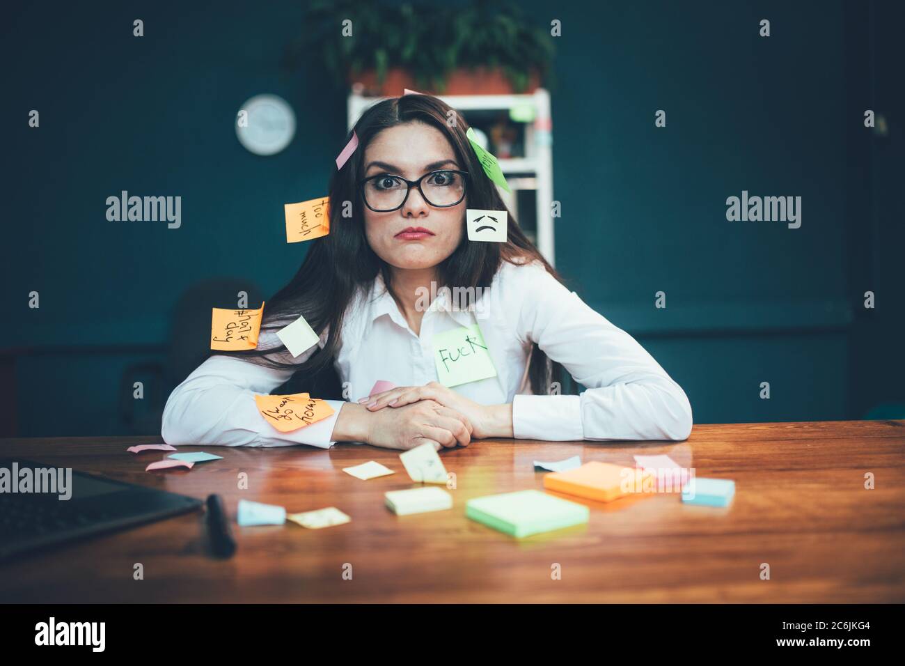Crazy woman with reminder labels sitting at office desk. Many memory stickers pasted on young Caucasian business woman. Multitasking concept. Deadline Stock Photo