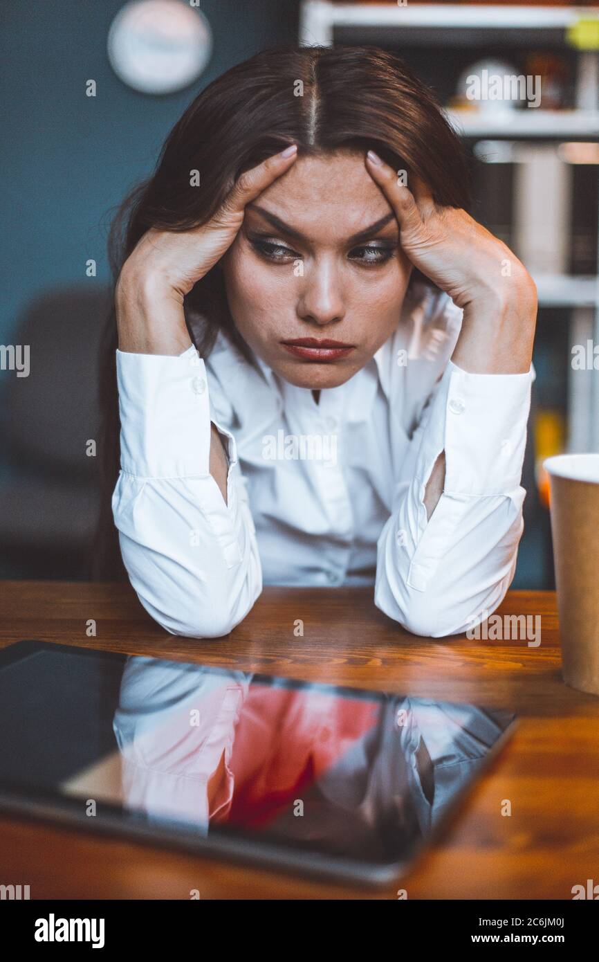 Exhausted business woman sits at workplace taking head in hands. Tired or bored female employee feels stress. Disappointment concept. Tinted image Stock Photo