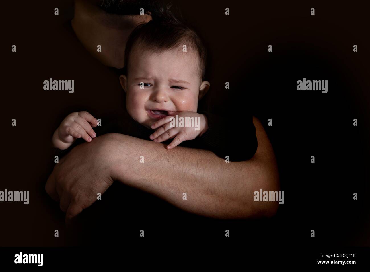men's hands holding crying baby in the black suit on the black background. Stock Photo