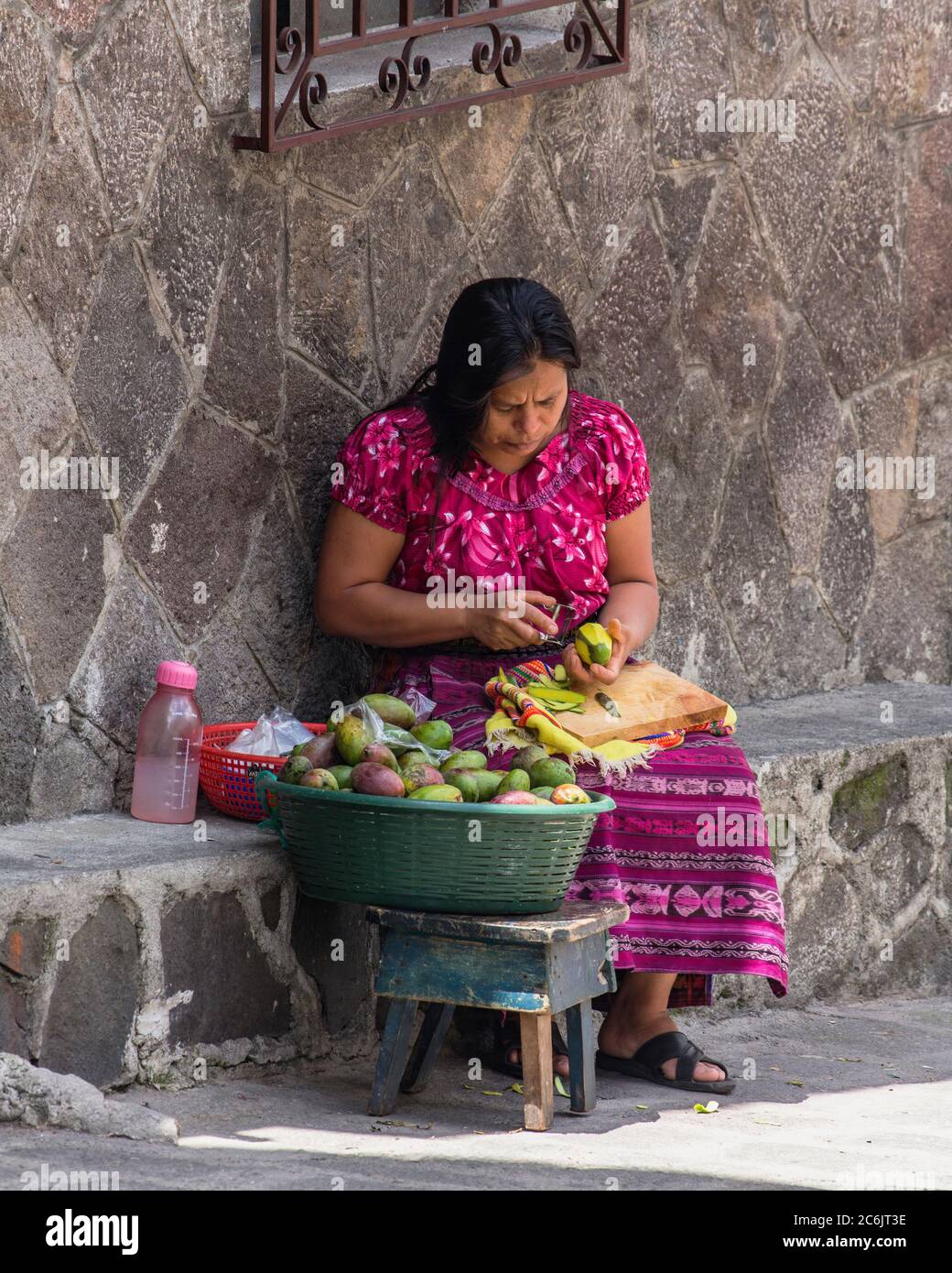 Guatemala, Solola Department, San Pedro la Laguna, A Mayan woman peels mangos on a street curb. Stock Photo