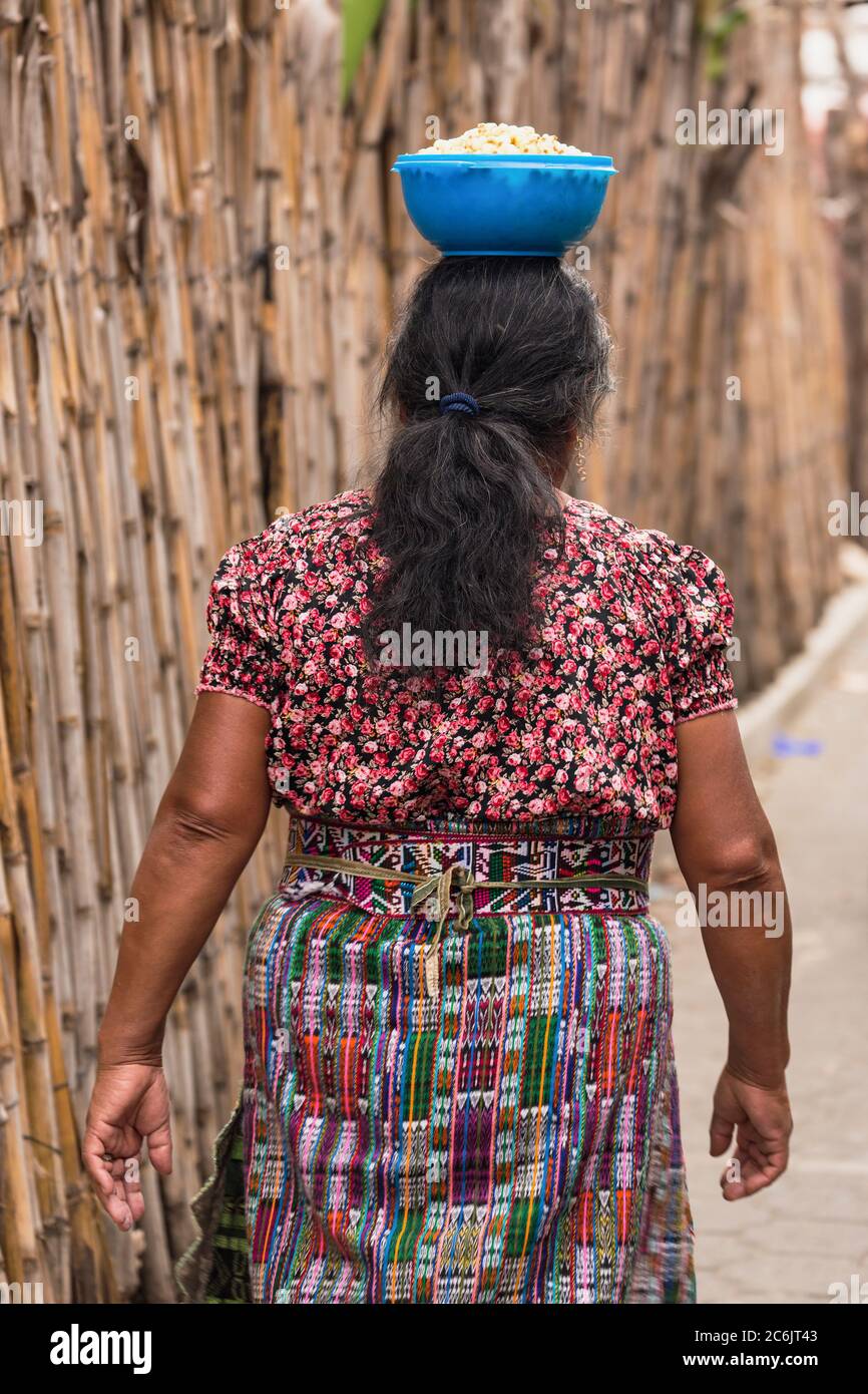 Guatemala, Solola Department, San Pedro la Laguna, A Mayan woman walks along a bamboo fencea with a bowl balanced on her head. Stock Photo