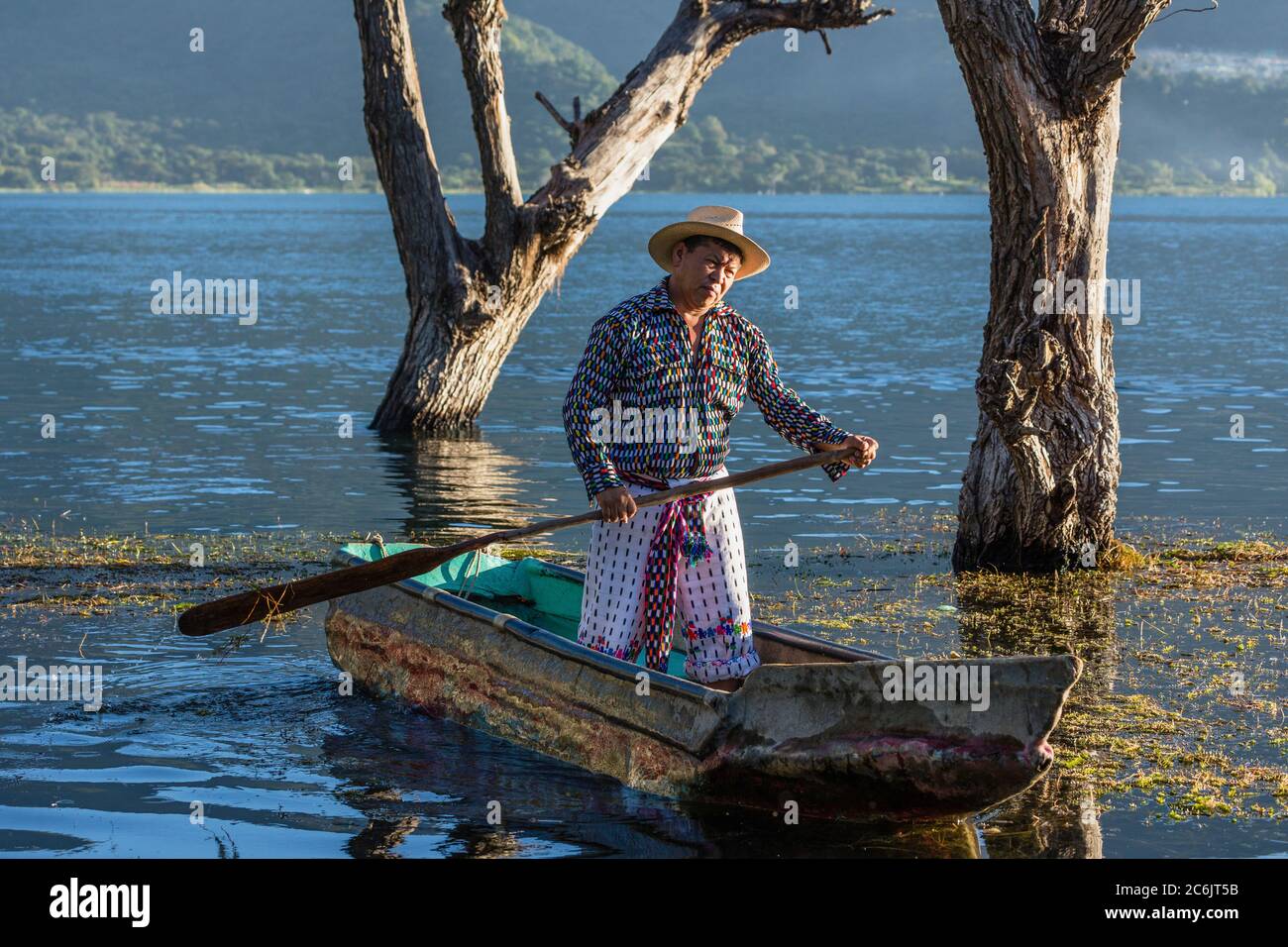 A Tzutujil Mayan man in the traditional dress of San Pedro la Laguna paddles his cayuco or fishing canoe on Lake Atitilan in Guatemala. Stock Photo