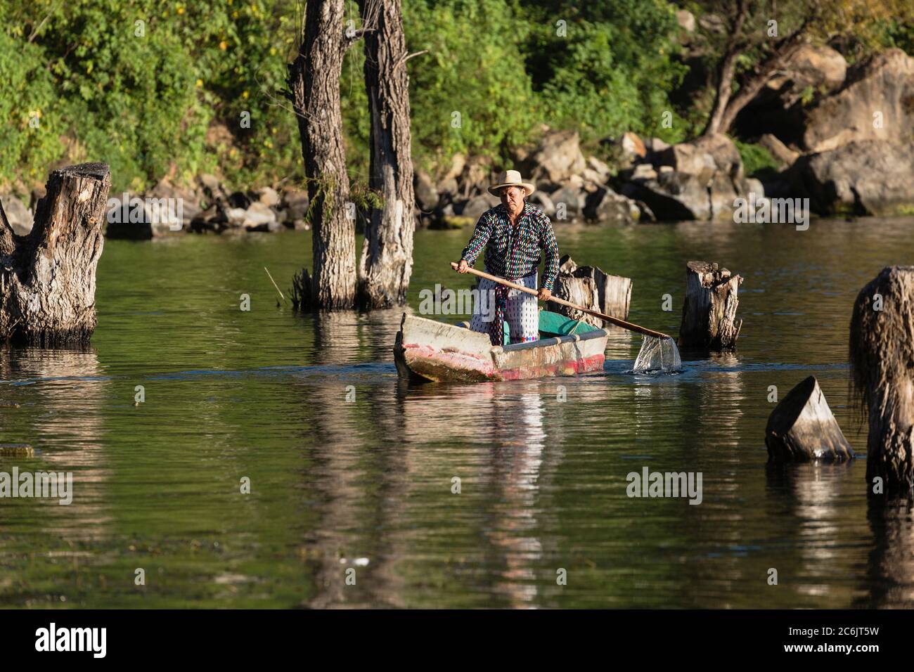 Guatemala, Solola Department, San Pedro la Laguna, A Tzutujil Mayan man in the traditional dress of San Pedro la Laguna paddles his cayuco or fishing canoe on Lake Atitilan. Stock Photo