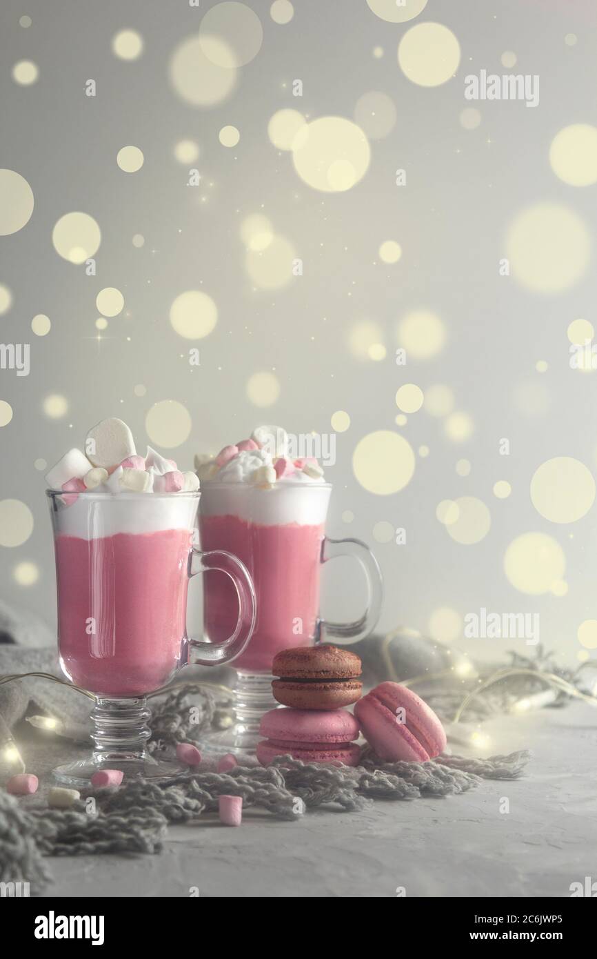 Pink hot chocolate with whipped cream and marshmallow candy in a 2 glass mugs, french macaroons and christmas lights. Copy space for text. Vertical Stock Photo