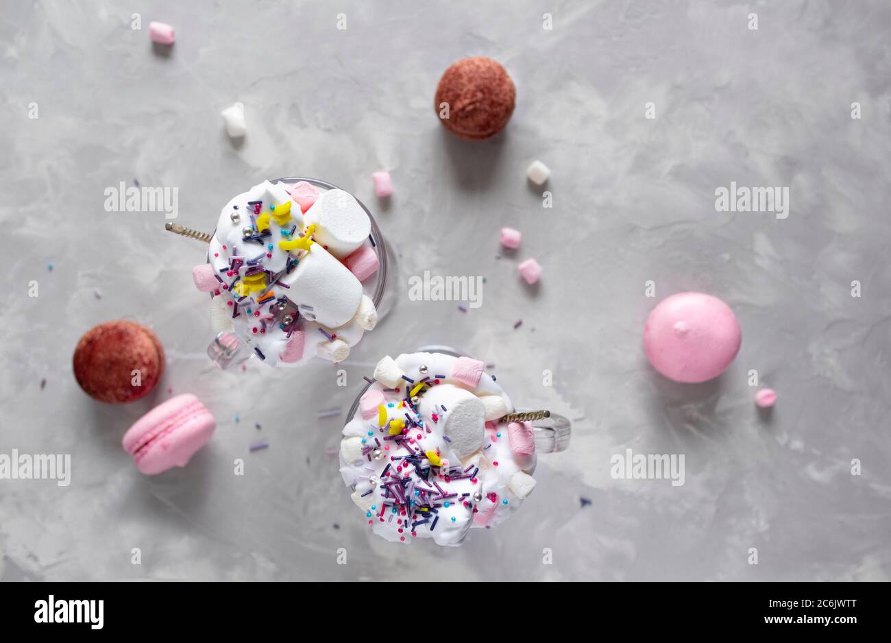 Pink hot chocolate with whipped cream and marshmallow candy in a 2 glass mugs, sweet pastel french macaroons on the grey background. Top view Stock Photo