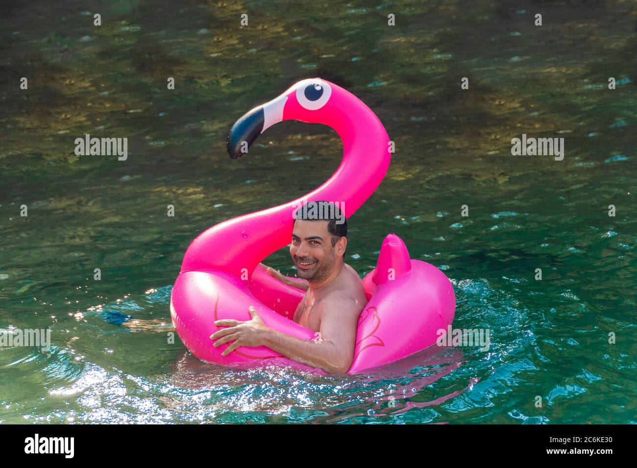 Cute and funny man enjoying on his inflated pink flamingo in sunny day. Stock Photo