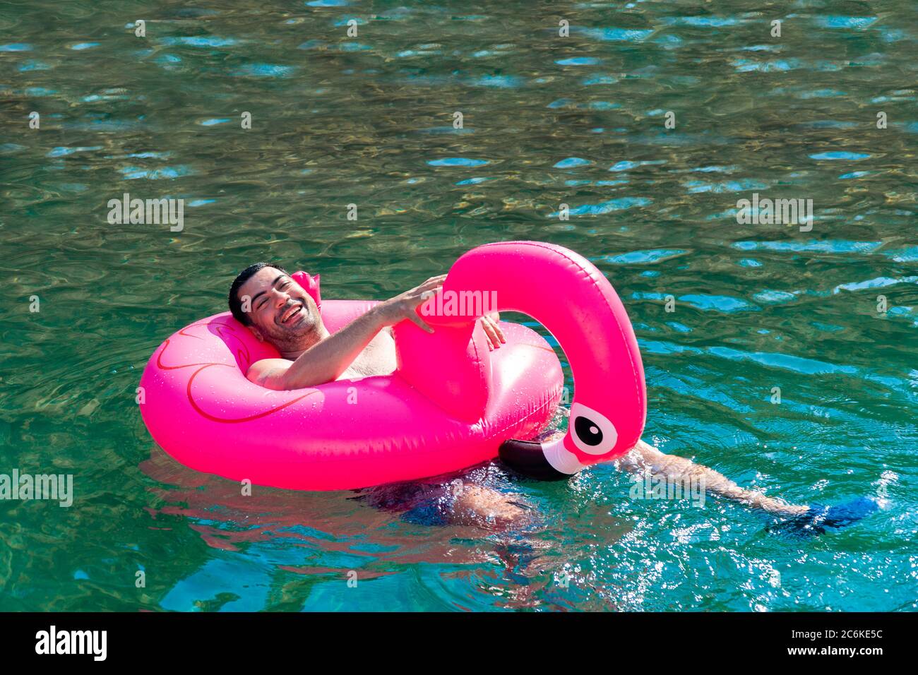 Cute and funny man enjoying on his inflated pink flamingo in sunny day. Stock Photo