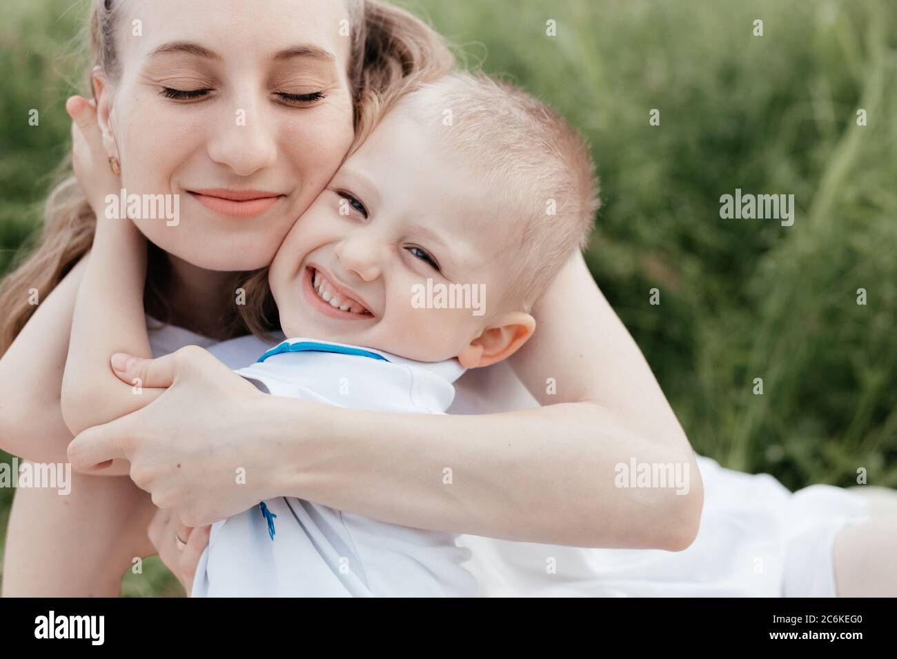 Smiling little boy embracing his happy mother who is sitting with closed eyes in nature. Mother and son. Happy family Stock Photo