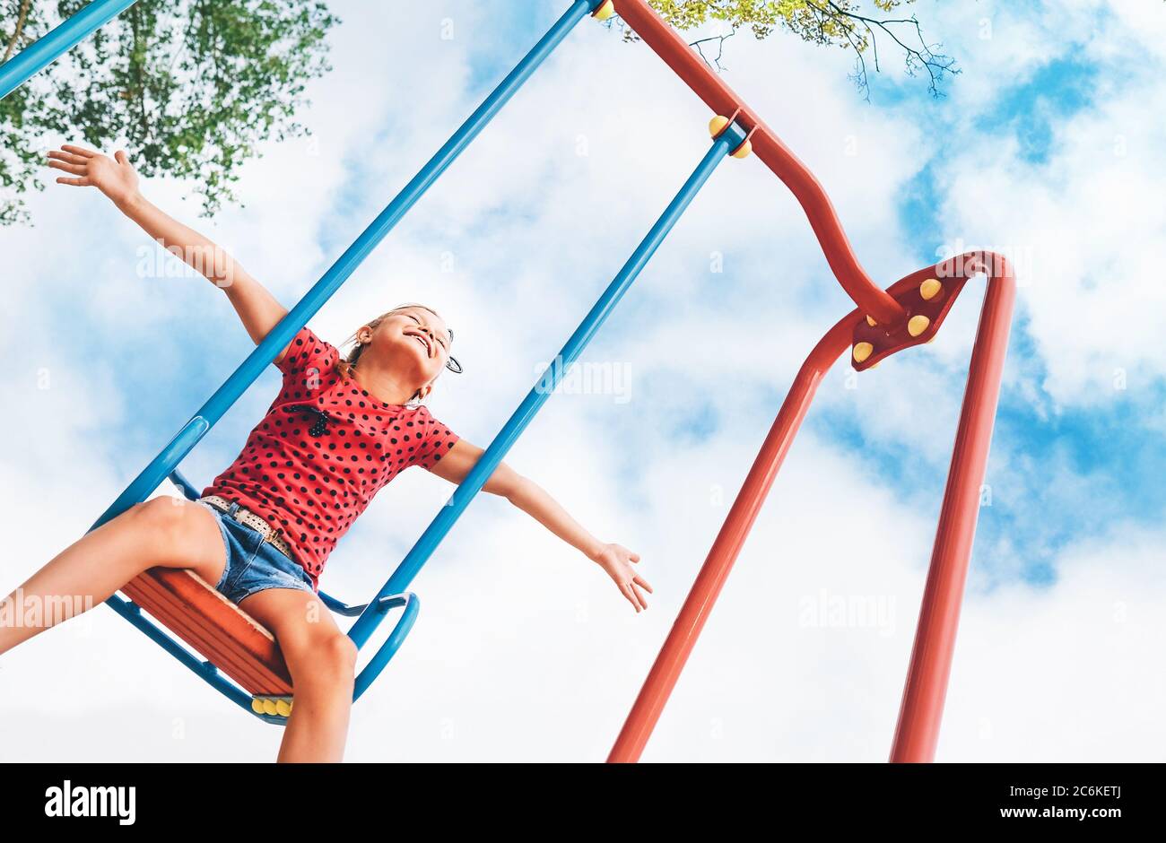 Funny smiling little girl swinging on the swing wide opened an arms