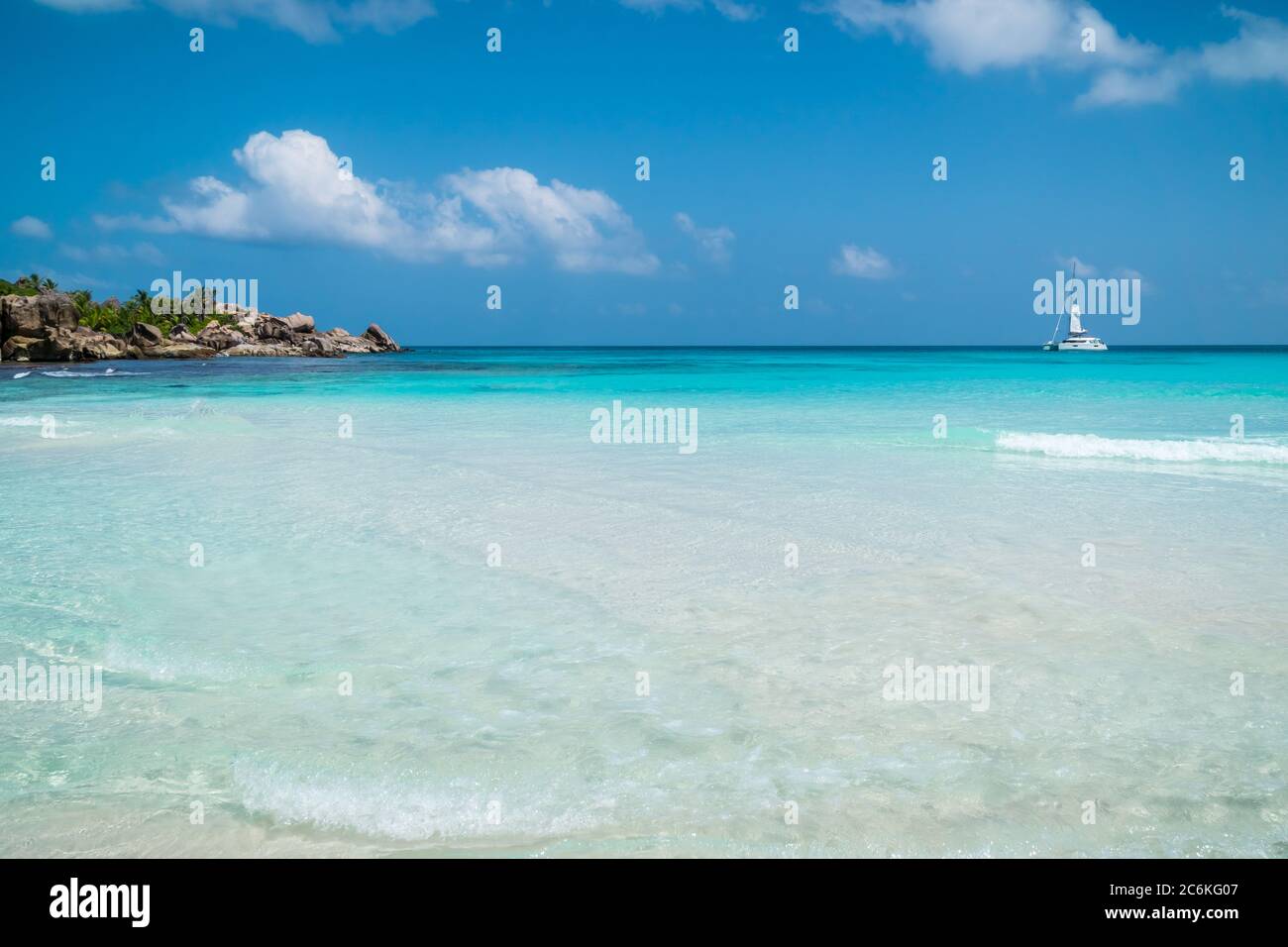 Ocean waves, white boat, pristine blue color lagoon and granite rocks on Anse Coco beach, La Digue Island, Seychelles Stock Photo
