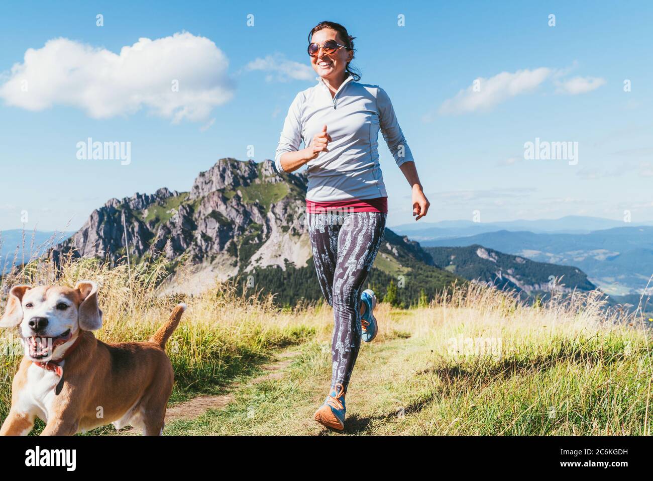 Happy smiling female jogging by the mounting range path with her beagle