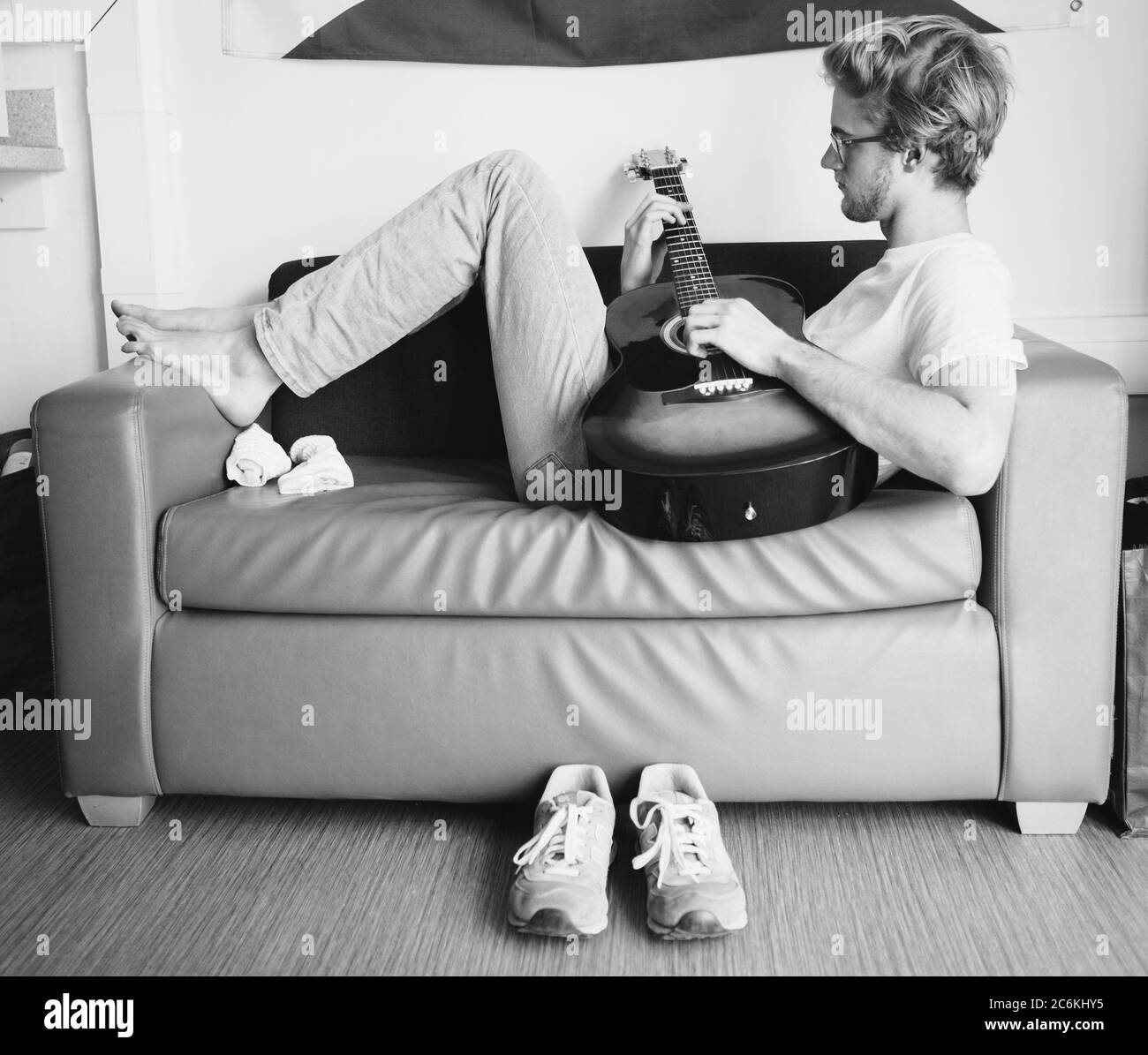 Black and white vintage image style of young man lying on sofa and playing on guitar in teen room. Stock Photo