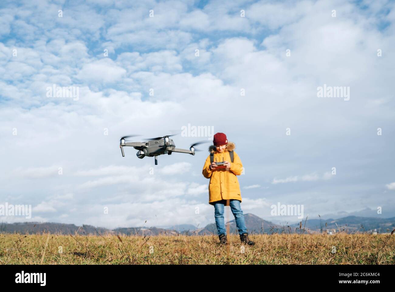 Teenager boy dressed yellow jacket piloting a modern digital drone using remote controller Stock Photo