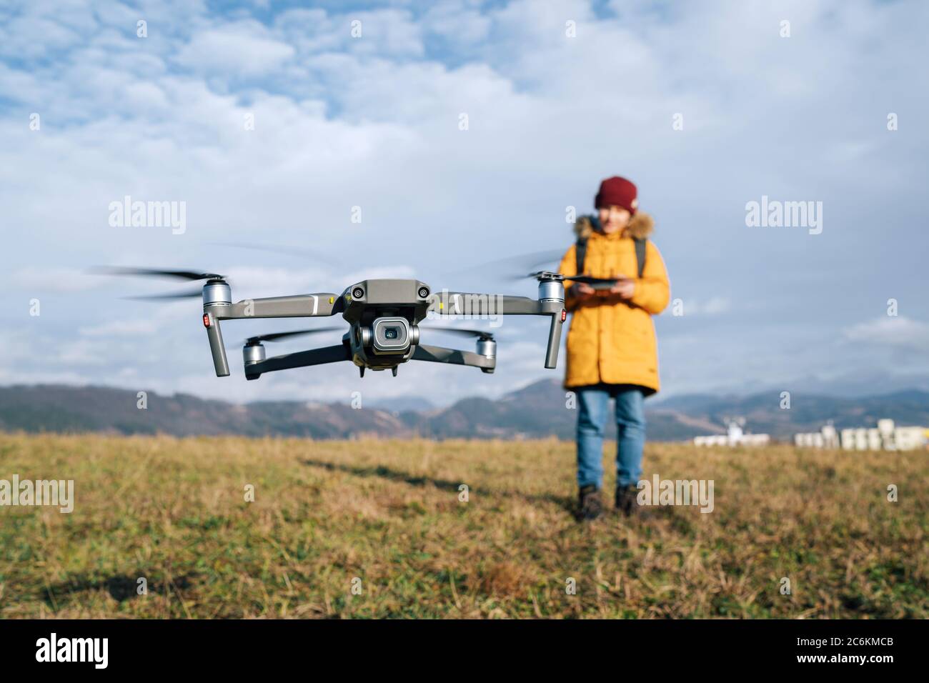 Close up image of flying drone with Teenager boy dressed yellow jacket  on background piloting a modern digital drone using remote controller Stock Photo
