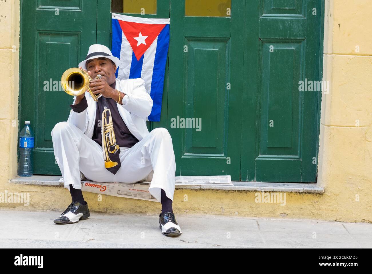 Cuban musician playing the trumpet next to a cuban flag in Havana Stock Photo