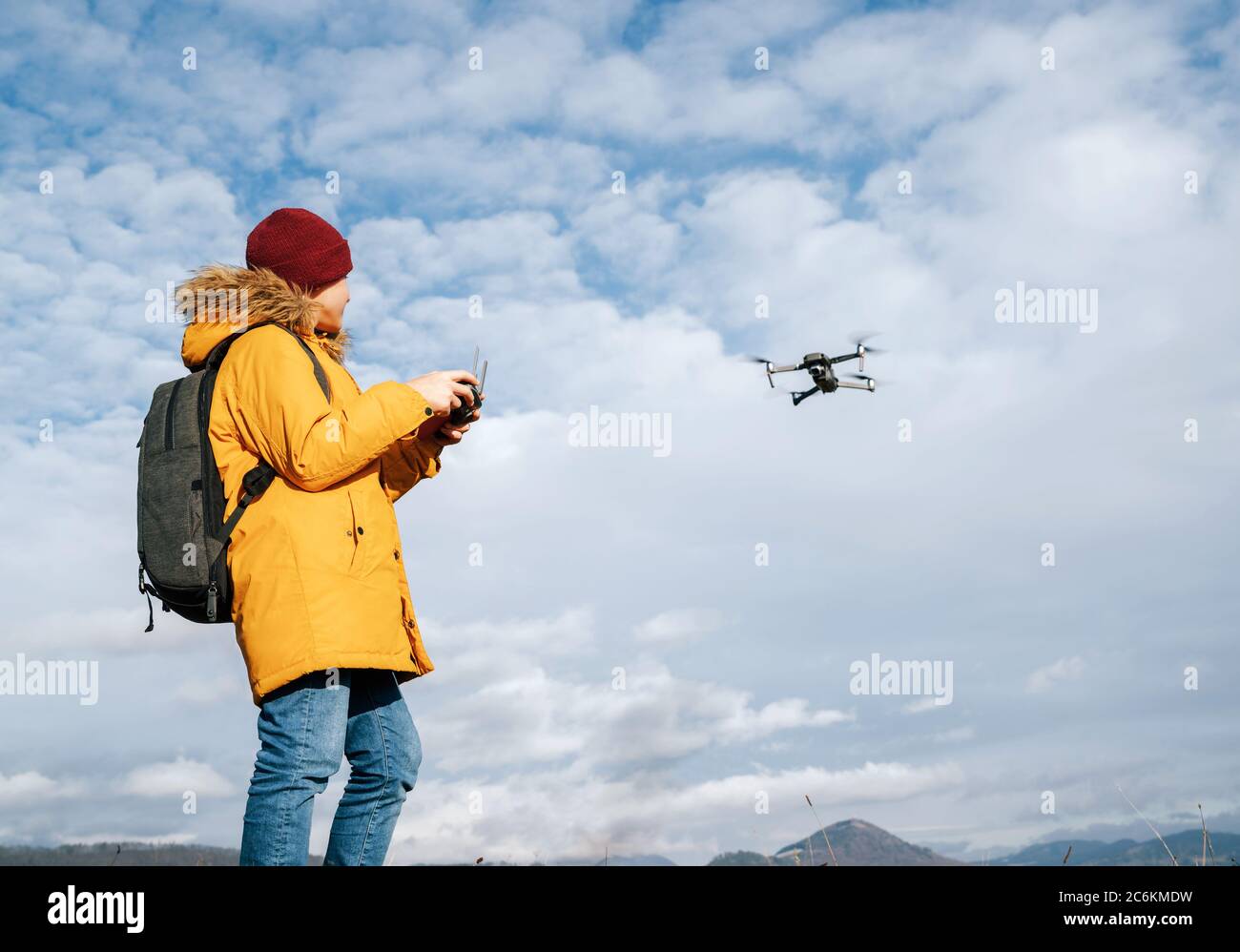 Teenager boy dressed yellow jacket piloting a modern digital drone using remote controller Stock Photo