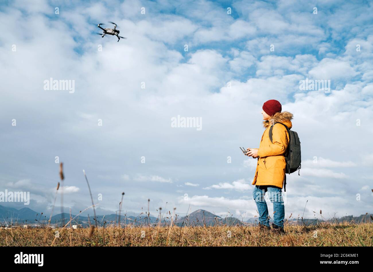 Teenager boy dressed yellow jacket piloting a modern digital drone using remote controller Stock Photo