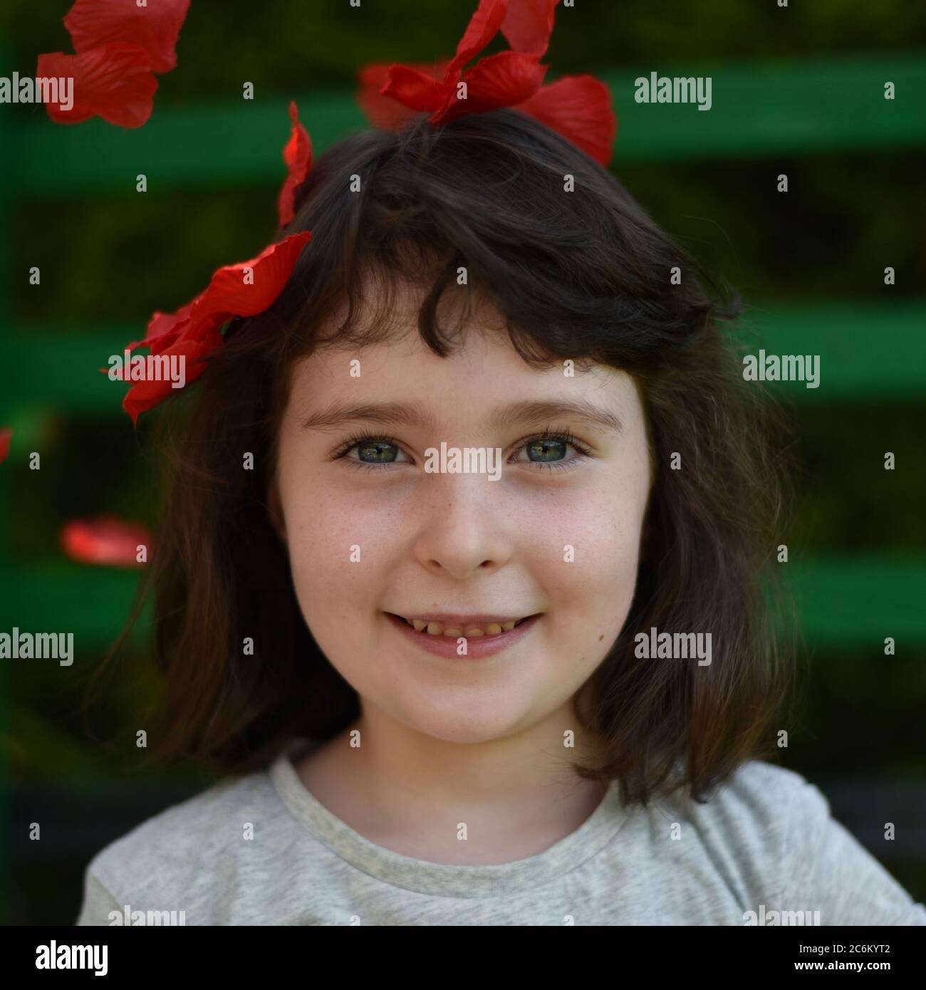 Portrait of little girl among red petals on a dark green background, square image Stock Photo