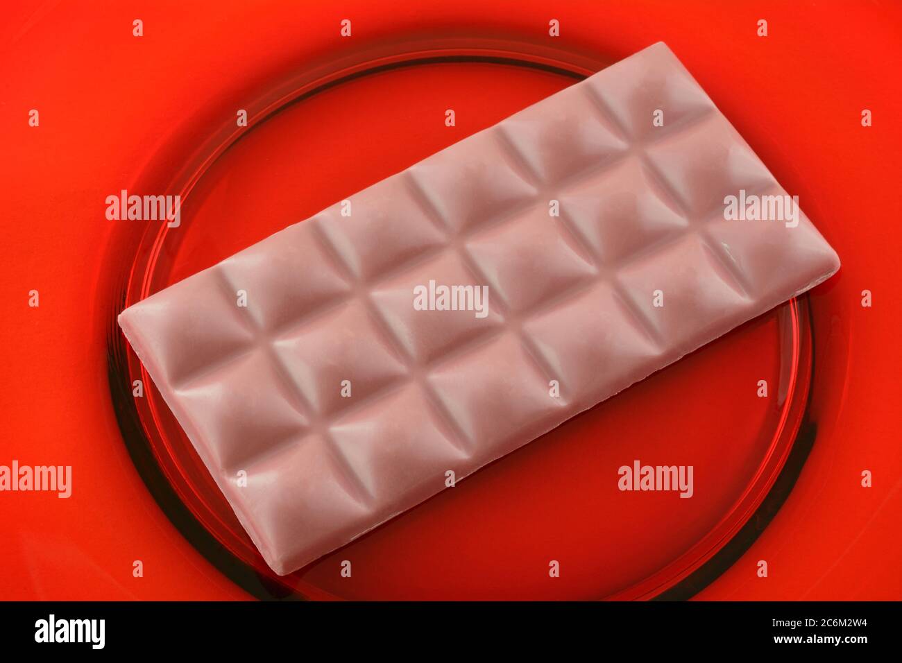 Closeup of ruby chocolate cacao snack bar on red glass plate Stock Photo