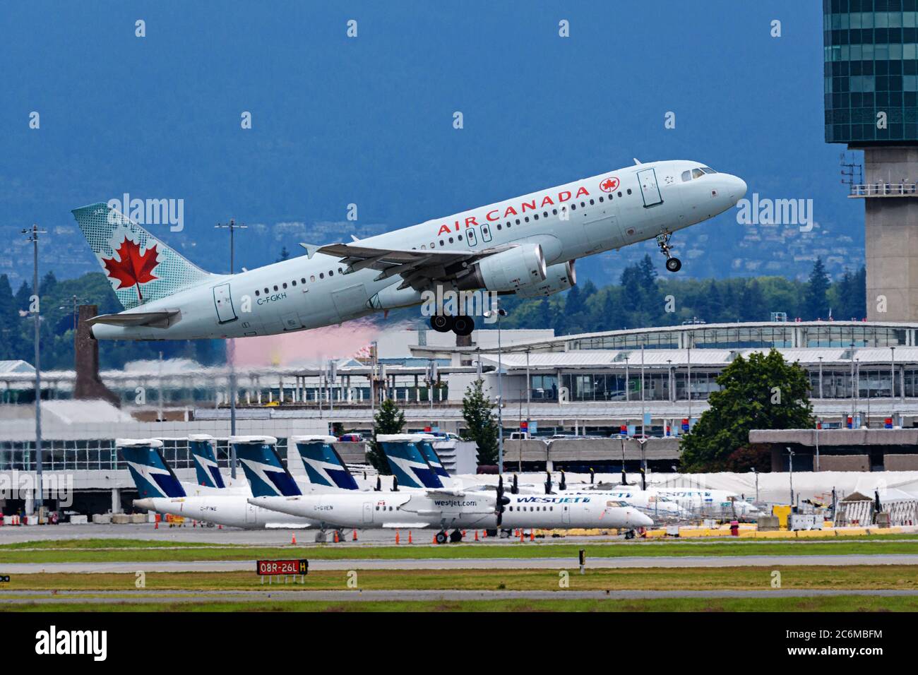 Richmond, British Columbia, Canada. 7th July, 2020. An Air Canada Airbus A320 jet (C-FGKH) takes off from Vancouver International Airport on a flight to Ottawa, July 7, 2020. In the background WestJet Encore Bombardier Q400 planes remain parked due to reduced air travel because of the COVID-19 pandemic. Credit: Bayne Stanley/ZUMA Wire/Alamy Live News Stock Photo