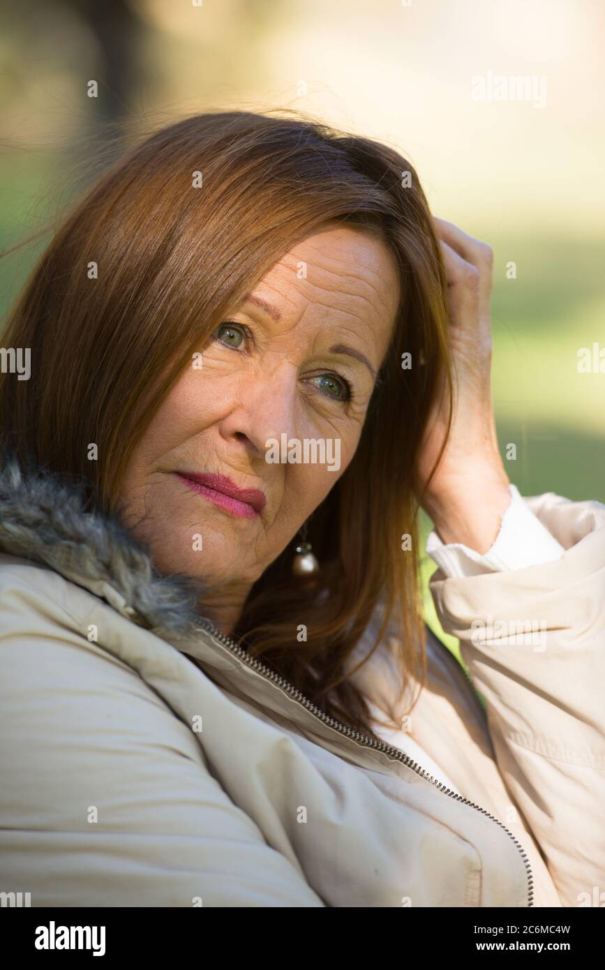 Portrait attractive mature woman sitting worried and thoughtful outdoors, blurred background. Stock Photo