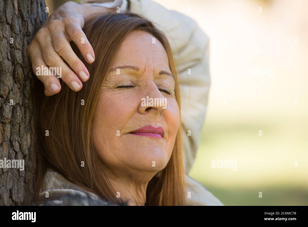 Portrait attractive mature woman relaxed in park with closed eyes, peaceful daydreaming, contemplating, thoughtful, blurred background. Stock Photo