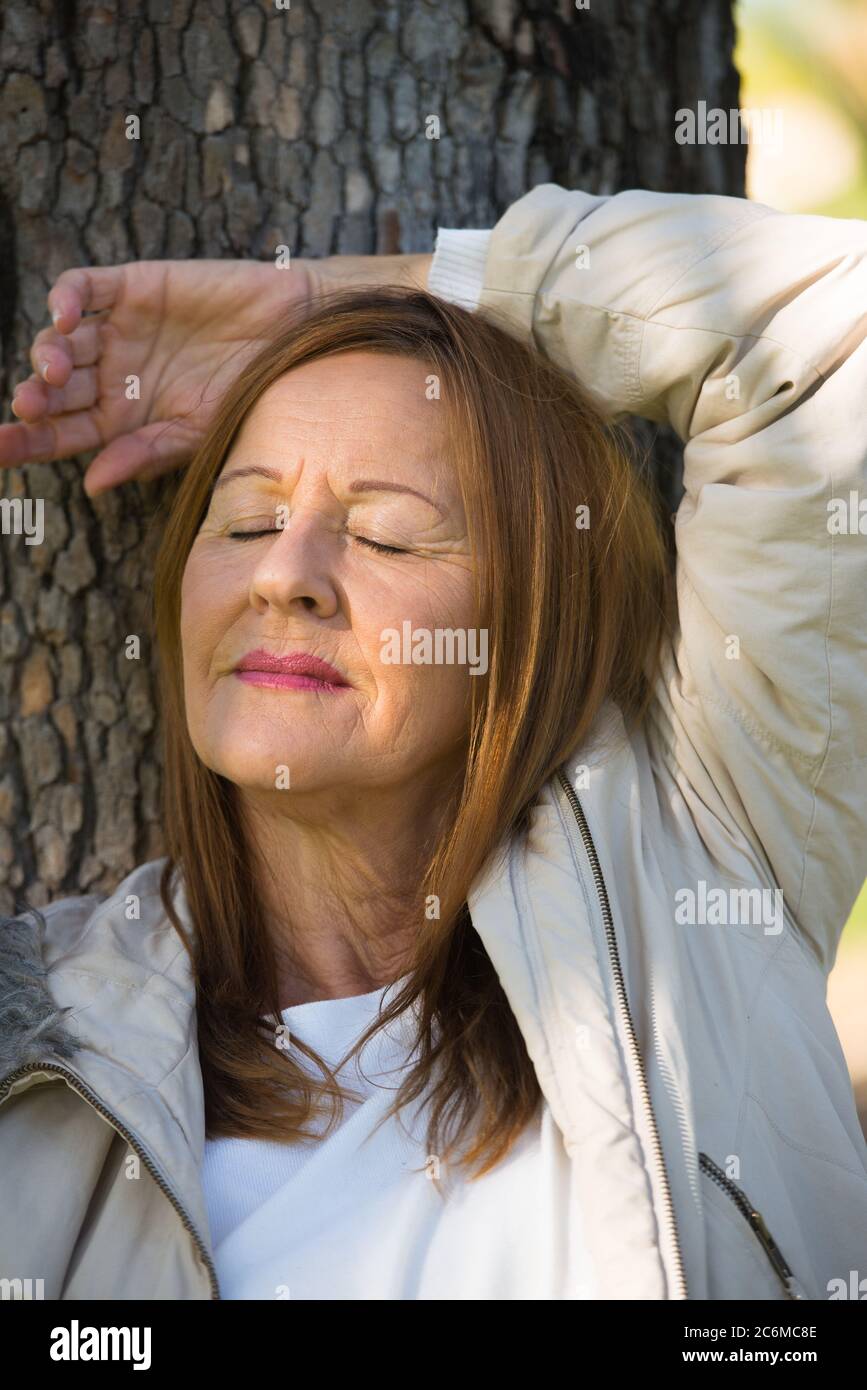 Portrait attractive mature woman relaxed in park with closed eyes, daydreaming, contemplating, thoughtful, blurred background. Stock Photo