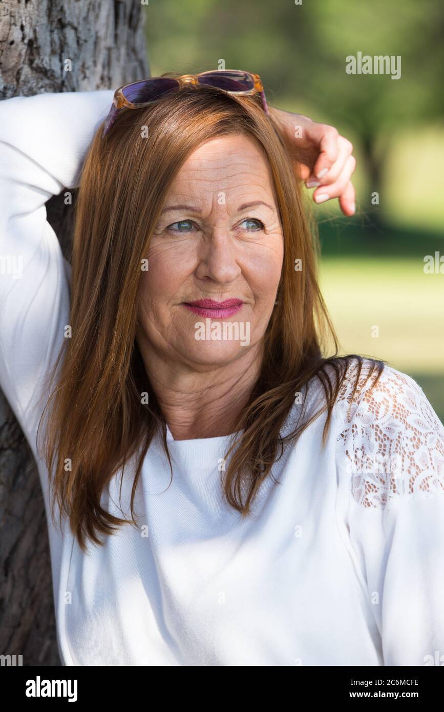Portrait attractive mature woman with long hair posing happy relaxed, thoughtful and confident outdoors in park, friendly smiling. Stock Photo