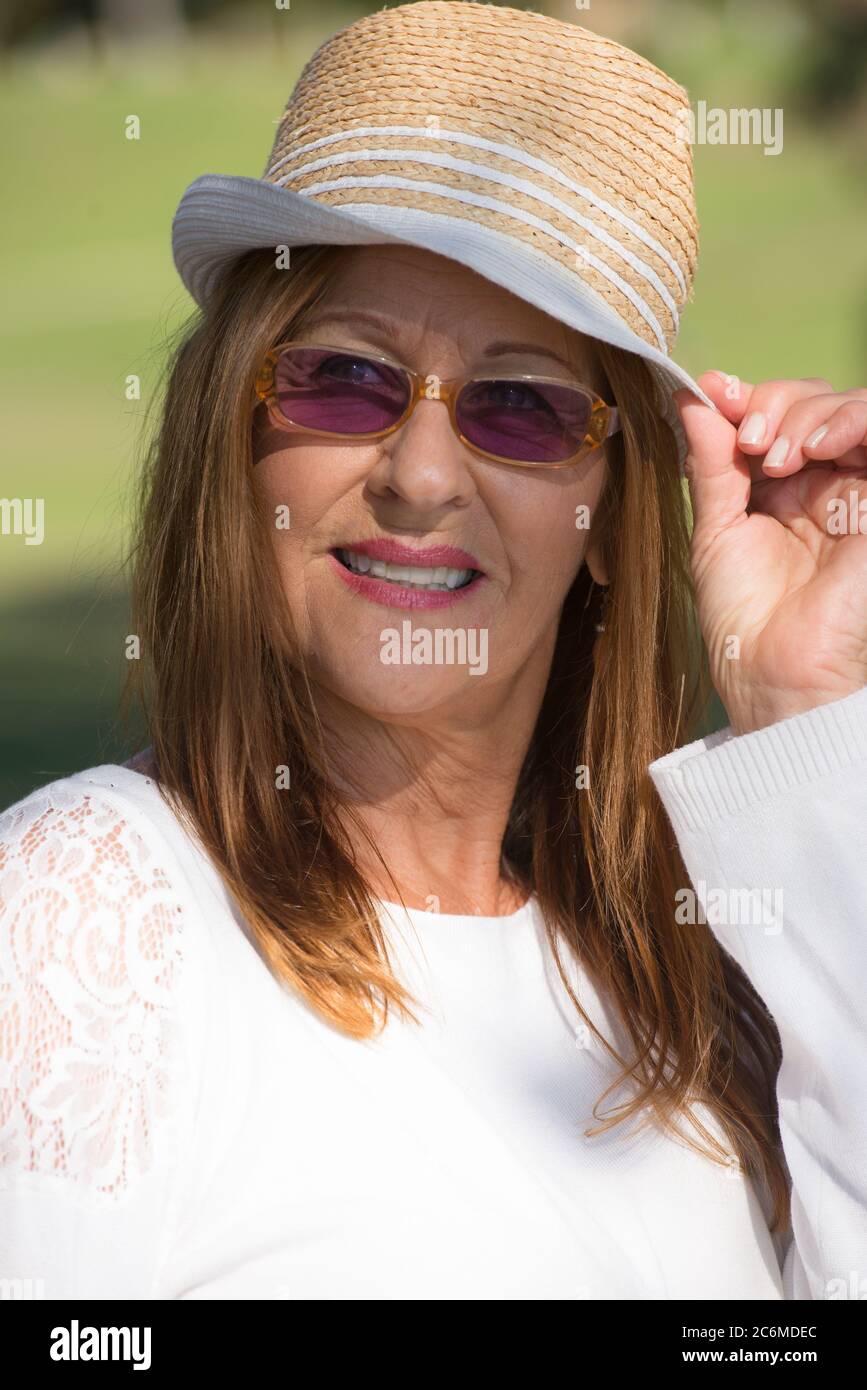 Portrait attractive mature woman in park, happy relaxed and thoughtful, wearing sunglasses and hat on summer sunny day. Stock Photo