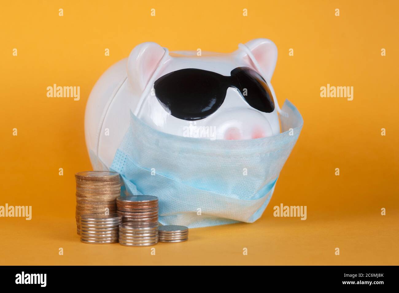 Covid-19 financial crisis. Coronavirus crisis, white piggy bank with face mask stuffed with coin on yellow background. Recession. Stock Photo