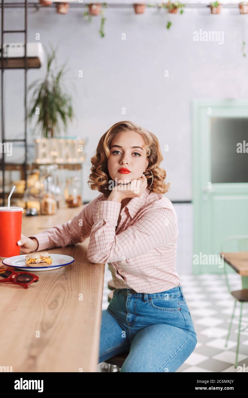 Young thoughtful lady in shirt and jeans sitting at the bar counter with  coca cola glass and dremily looking in camera in cafe Stock Photo - Alamy